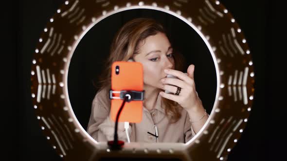 View of Woman Fashion Blogger Contouring Face in Front of Ring Light with Phone