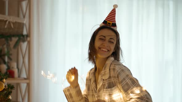 Happy Joyful Pretty Woman Wearing Reindeer Antlers Headband Dancing with Christmas Lights at Cozy alt