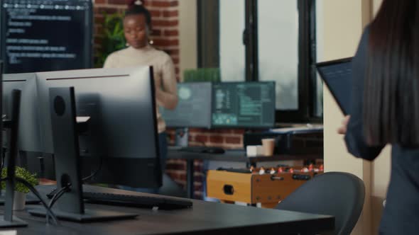 Two Software Developers Coming at Desk and Sitting Down Holding Laptop with Coding Interface alt