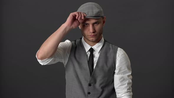 Portrait of Dangerous Gangster Guy in Suit and Flatcap Posing on Camera with Hands Folded and alt