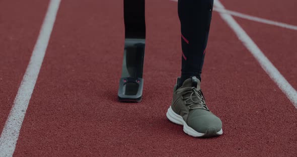 Crop View of Disabled Male Person with Prosthetic Running Blade Walking and Stopping at Sports Field alt
