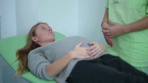 Young Focused Pregnant Woman Listening to Unrecognizable Doctor Lying on Examination Couch in alt