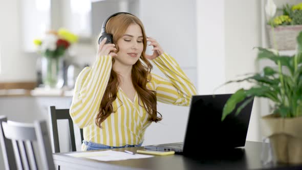 Young woman putting on headphones for video call over laptop