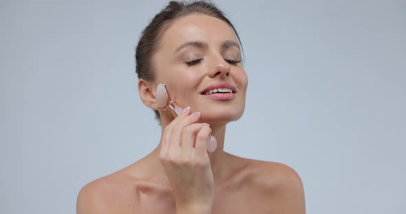 Young Woman Using Jade Facial Roller for Skin Care Beauty Treatment on Gray Isolate Background alt