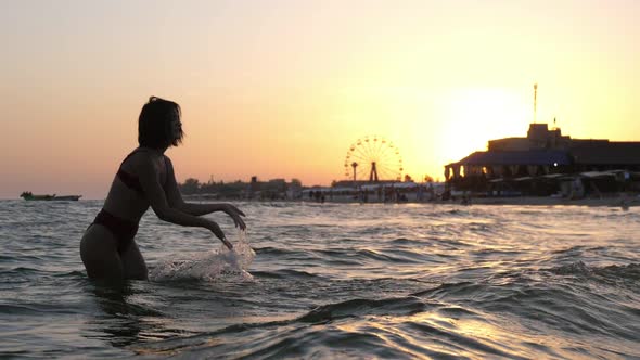 Happy Brunette Girl in Bikini Splashing Water on River Beach in Slow Motion