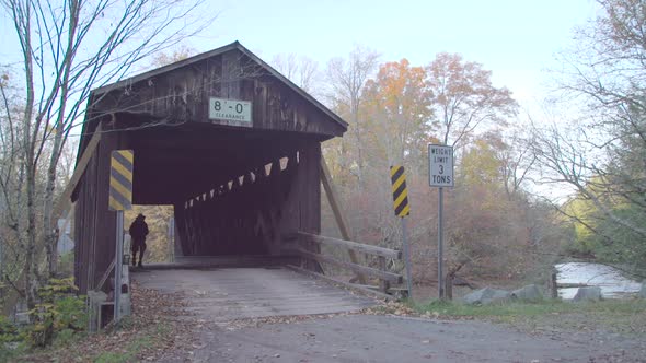 An older man crossing an old wooden bridge while on a scenic hike through a forest in the mountains. alt