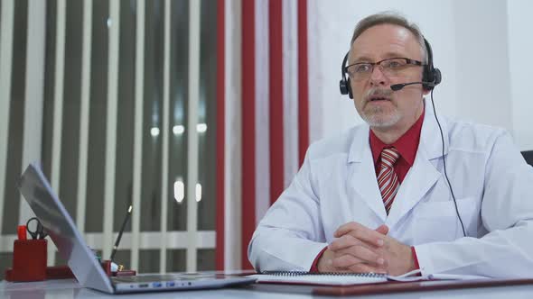 Doctor with headset talking on camera in medical office.  alt