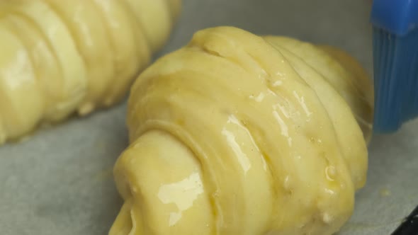 Close Up Spreading of Egg Yolk on Italian or French Croissants with Silicone Brush Laying on Bakery alt
