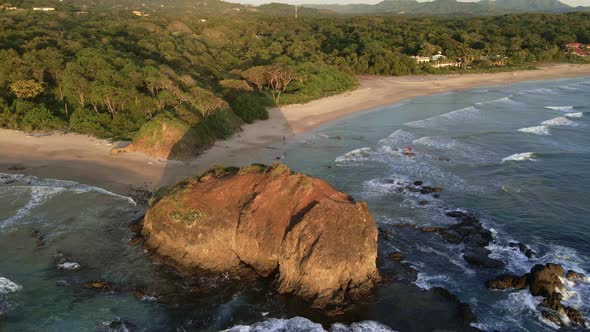 Large beach rock during sunset in Costa Rica. 4k aerial footage of a tropical paradise being illumin alt