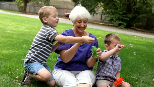 Senior woman and two young boys blowing bubbles alt