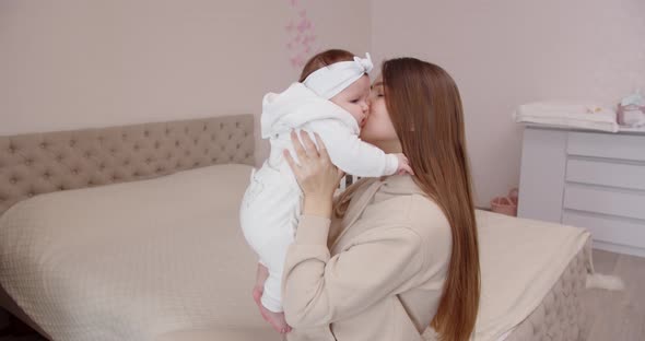 A Smiling Young Mother Gently Touches The Face Of Her Newborn Baby, Holding Her In Her Arms