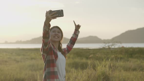 Attractive young Asian woman selfie video chat with her friends on the smartphone while sunset.