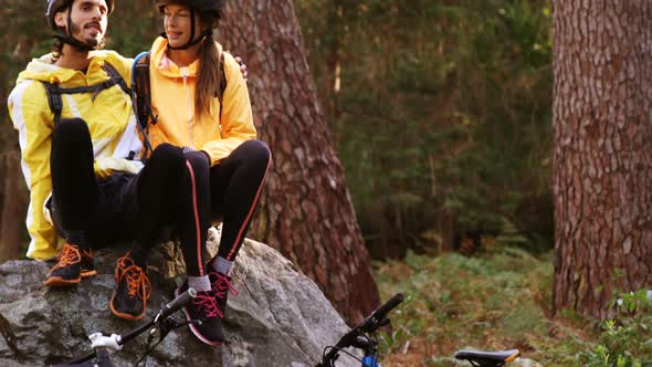 Mountain biking couple sitting on a rock in the forest alt