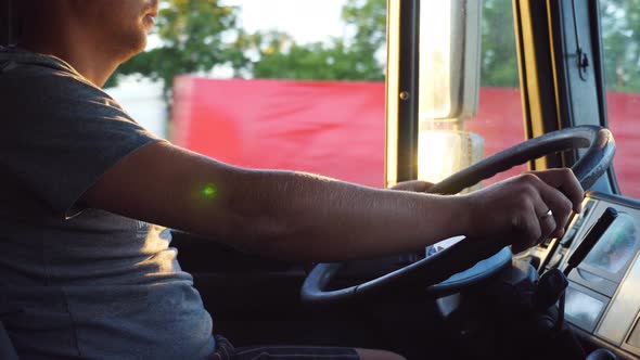Man Holding His Hand on the Steering Wheel and Driving a Truck at Country Road on Sunny Summer Day alt