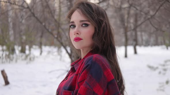 Young Woman with Wavy Hair Standing and Touching Face in Winter Forest