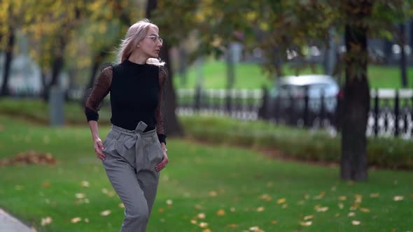 Sexy Blonde Woman Is Walking on Street of City at Early Autumn, Moving Passionately and Smiling alt