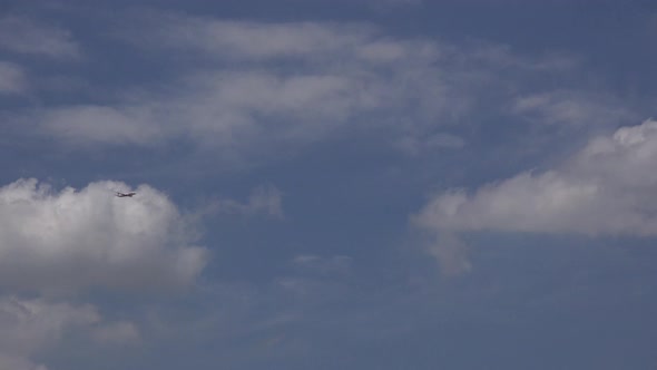 An airplane flies across a blue sky with white clouds.