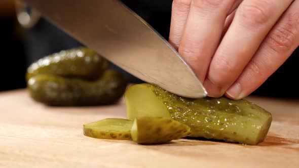 Hands is Cutting a Pickled Cucumber with a Knife on Wooden Board Closeup