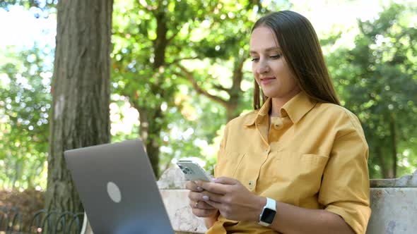 Side View at Female Student Wearing Yellow Casual Shirt Texting on the Smartphone and Using Laptop