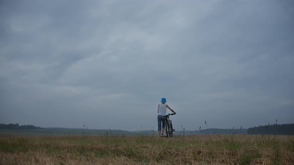 Boy in the Field with a Bicycle in Rainy Weather