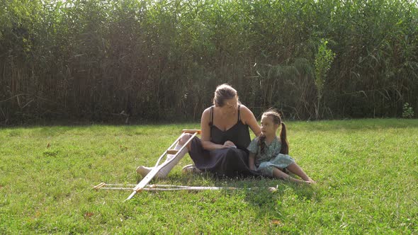 A Young Girl with a Cast and a Walker is Sitting on the Lawn in the Park and Talking to a Little alt