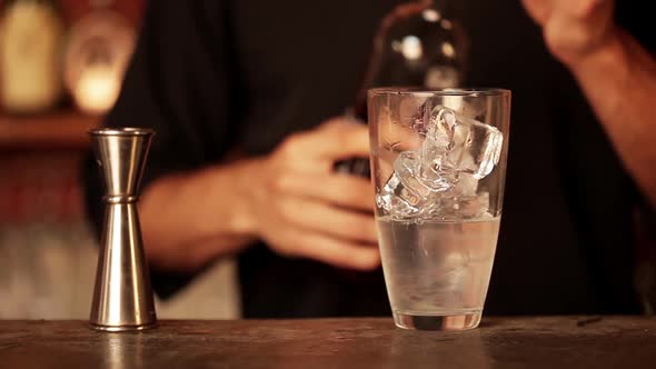 Bartender adding shot of cranberry juice to cocktail mixture in shaker alt