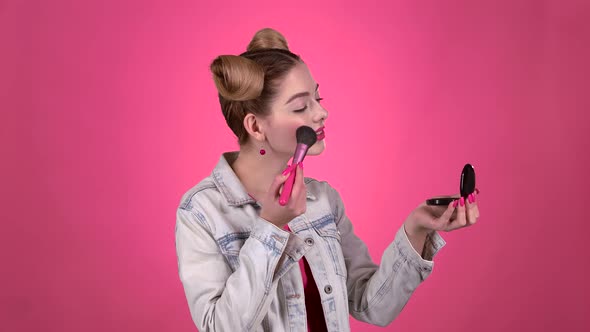Girl Holding a Brush in Her Hand and Powdering Her Face. Pink Background. Slow Motion alt