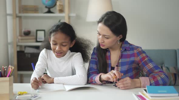 Medium Shot of Asian Happy Woman Tutor Teaching and Helping Her Black African American Girl Student alt