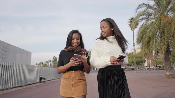 Girls walking in a city while using a mobile phone and laughing alt
