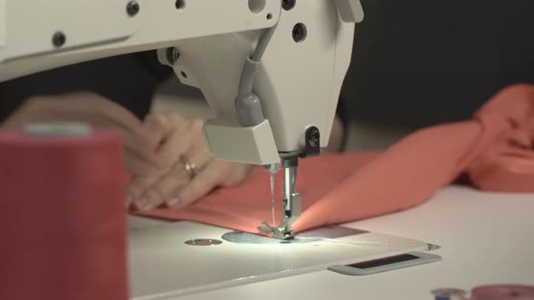 Close Up Footage of Sewing Machine Stitching Piece of Peachcolored Fabric While Woman's Hands alt