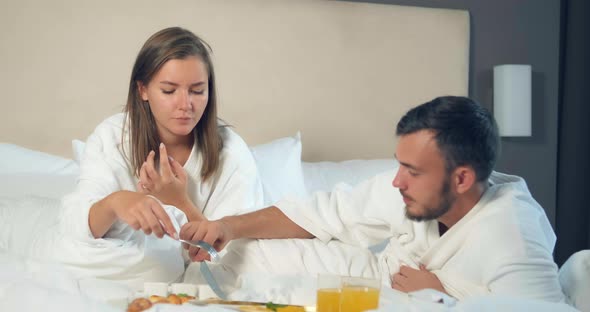 Man Cuts Food on Tray for Girlfriend Having Breakfast on Bed alt
