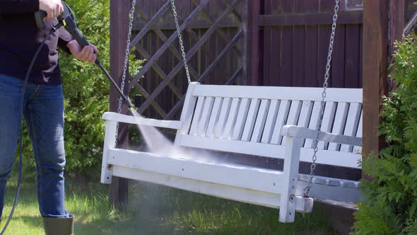 Male Gardener Removes White Paint From a Swing Bench with High Pressure Washer alt