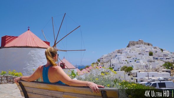 4K Young Woman Admiring the View of Astypalea Island from a Park Bench, Greece, Europe alt