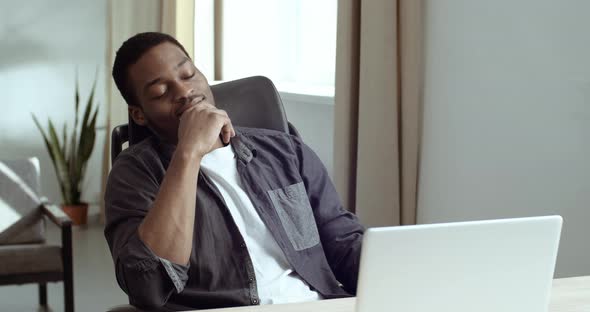 Tired Afro American Guy Student Business Man Sitting at Workplace in Front of Laptop Feels Stress alt