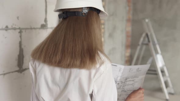 The girl engineer builder is checking the drawings at the apartment of the projected house. alt