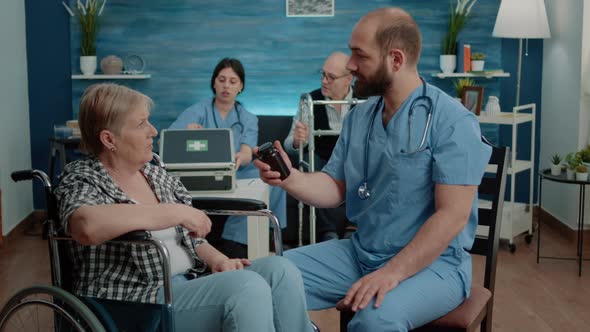 Man Nurse Giving Bottle of Pills to Old Patient with Disability alt