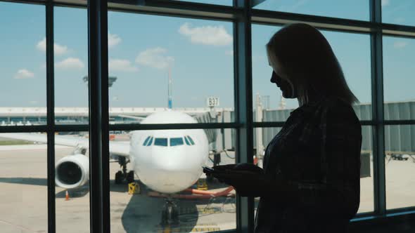 Silhouette of a Business Woman By the Window of an Airport Terminal. Uses a Smartphone alt