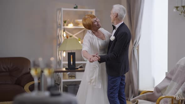Wide Shot Happy Senior Couple of Newlyweds Dancing in Slow Motion Indoors Smiling alt
