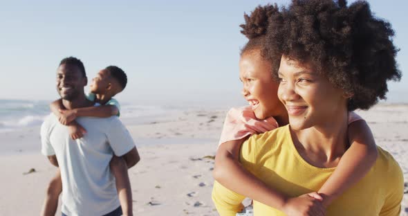 Smiling african american family embracing and walking on sunny beach alt