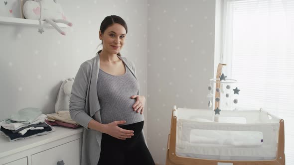 Thoughtful caucasian woman in advanced pregnancy standing in the baby's room next to the crib. Shot alt