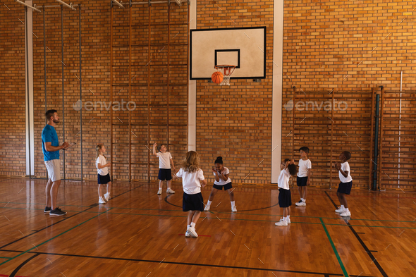 Basketball coach teaching to schoolkids at basketball court in school Basketball coach teaching to schoolkids at basketball court in school