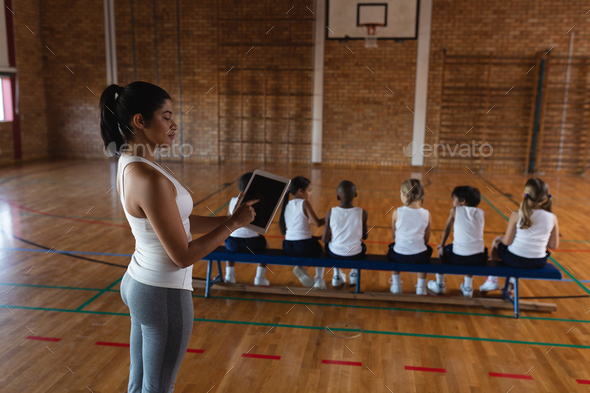 Side view of female basketball coach using digital tablet at basketball court in school