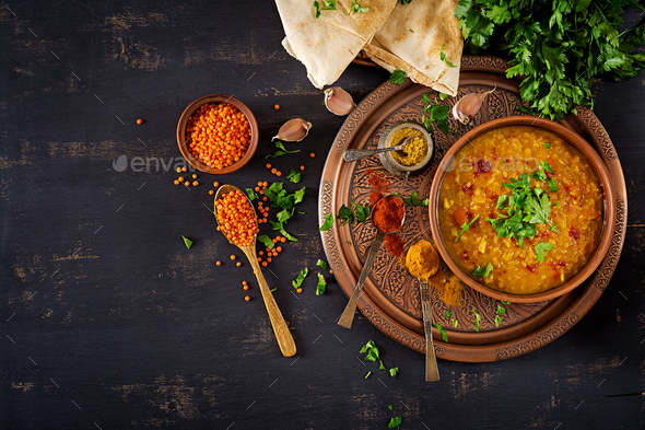 Indian Dhal spicy curry in bowl, spices, herbs, rustic black wooden background.