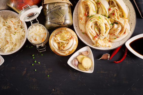 Cabbage kimchi, tomatoes marinated, sauerkraut sour glass jars over rustic kitchen table.