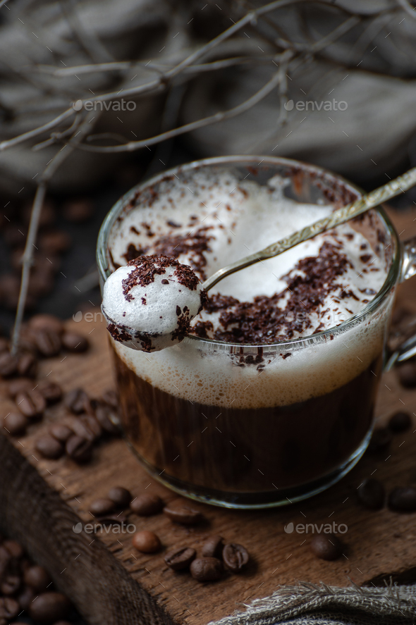 Cappuccino with milk foam in a spoon on a wooden board closeup. - Stock Photo - Images