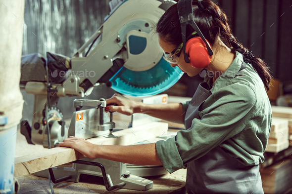 Busy and serious craftswoman grinding timbers with special machine. - Stock Photo - Images