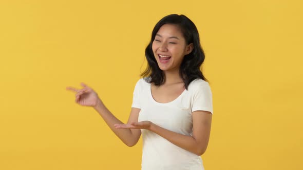 Beautiful smiling young Asian woman opening palms and pointing her finger to copy space