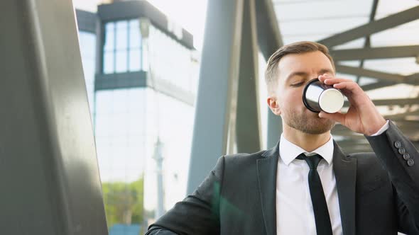 Young Confident Businessman Drinking Coffee and Looking at Camera Near Business Center alt