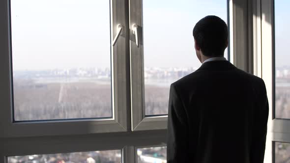 Back View of Young Successful Businessman Standing in Front of Windows Looking Into Distance on the