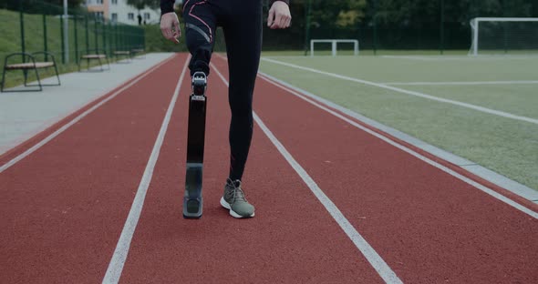 Crop View of Disabled Male Person Legs with Prosthetic Blade Walking at Sports Field alt